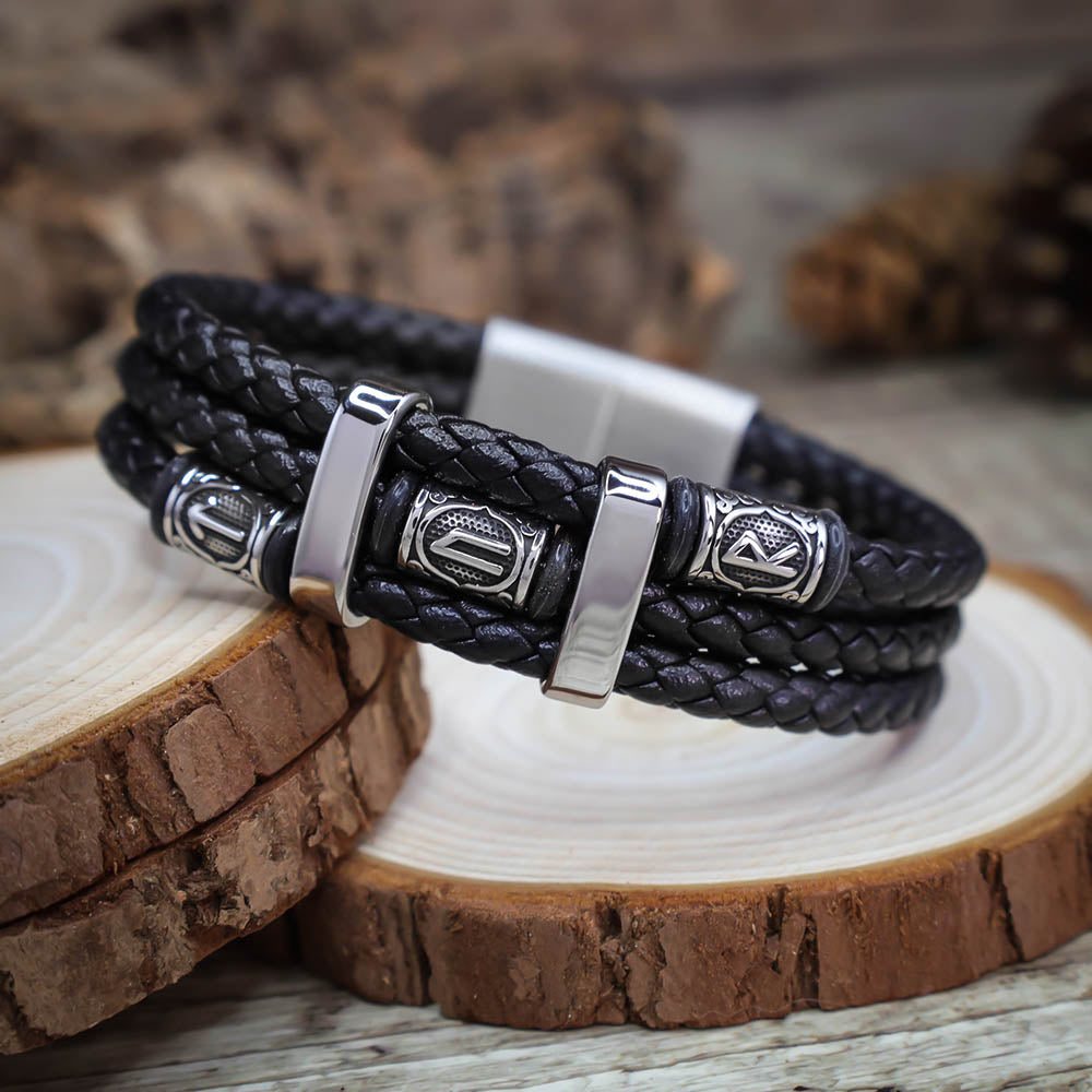 Black braided leather bracelet with silver metal clasps on a wooden surface