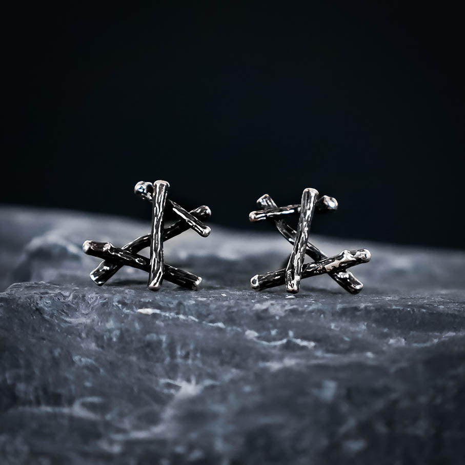 Silver twig-shaped earrings on a dark stone surface