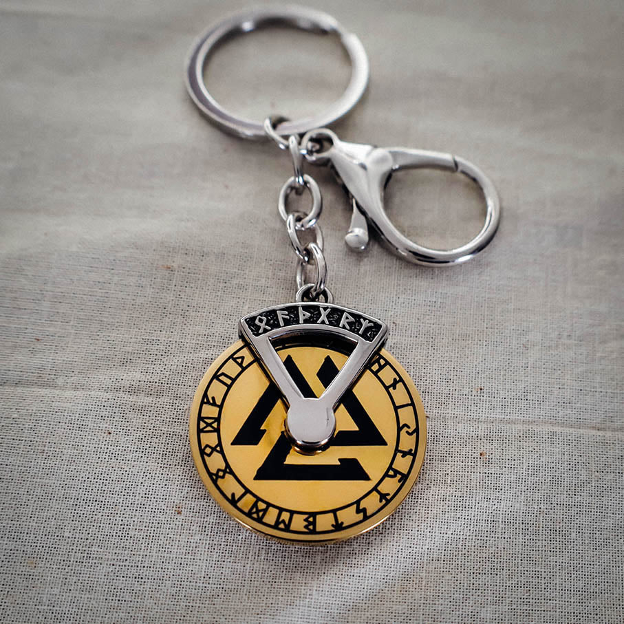 A stainless steel keychain featuring a gold-colored spinner disk with Norse runic symbols, on a grey background.