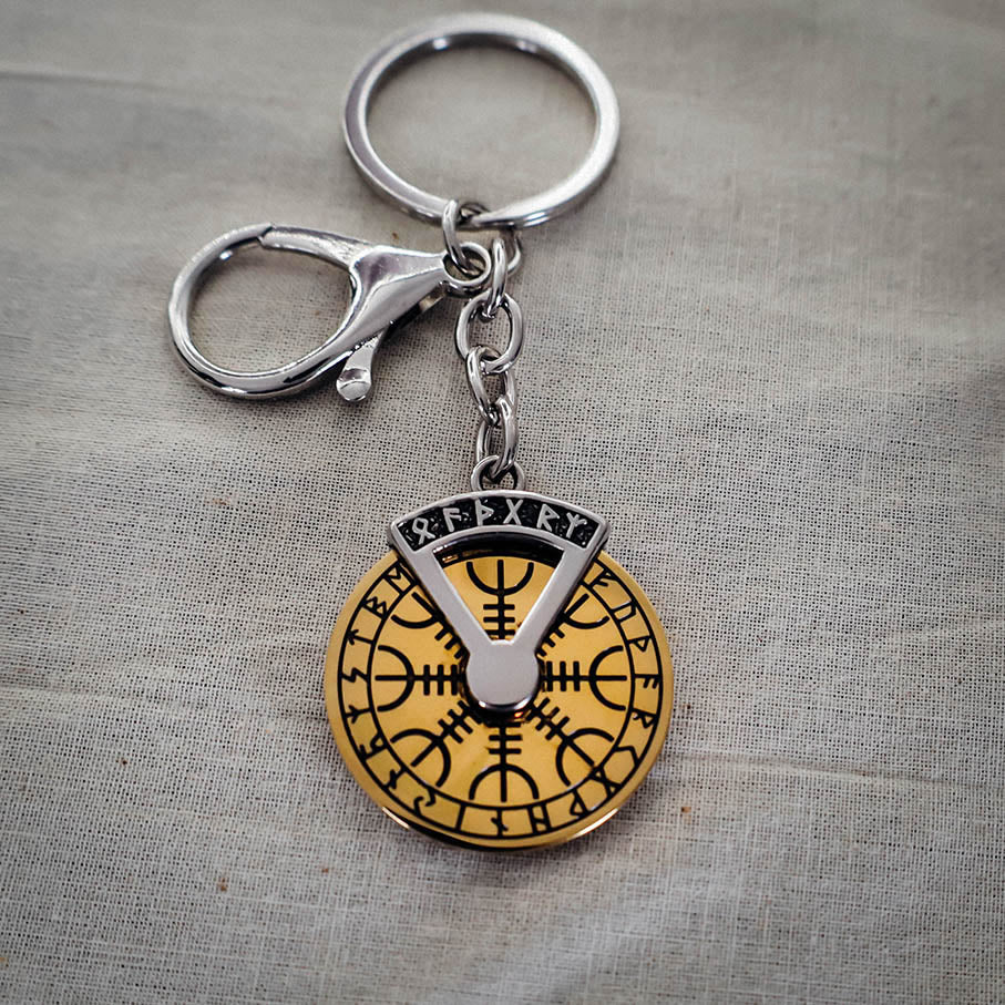 A stainless steel keychain featuring a gold-colored spinner disk with Norse runic symbols, including Valknut and Helm of Awe, on a grey background.