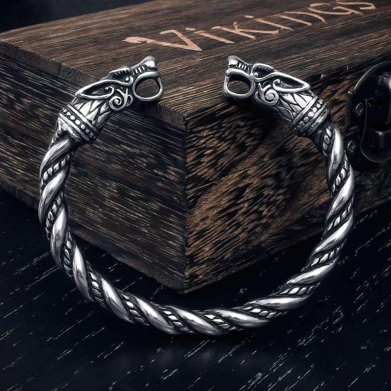 A stainless steel Viking bracelet with twisted wire design and wolf head end-piece adornments, displayed on a wooden surface.