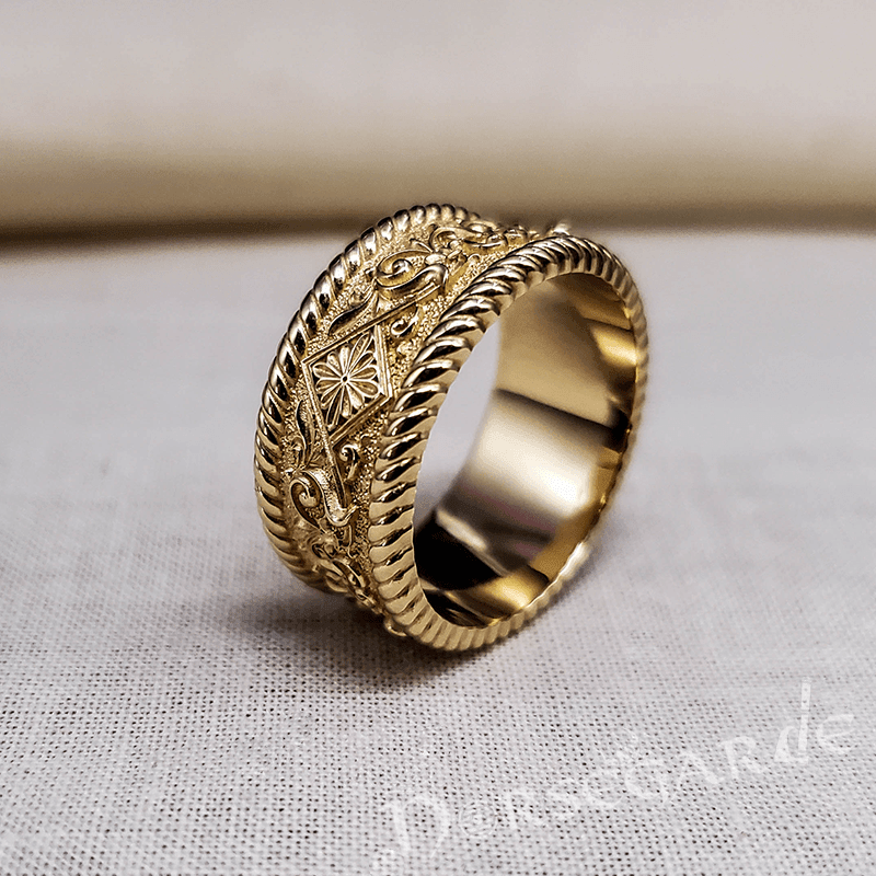A gold-colored handcrafted Norse floral ornament band ring with engraved patterns, displayed on a textured fabric surface.