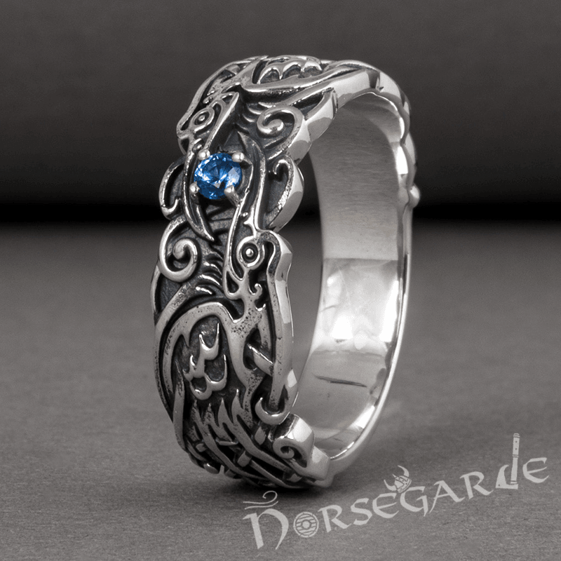A handcrafted sterling silver ring featuring Norse art stylized Odin's ravens with a gemstone embedded on the band.