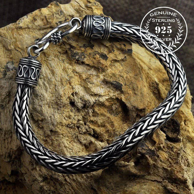 A sterling silver Viking scale bracelet with hook and end-piece adornments, displayed on a rock.